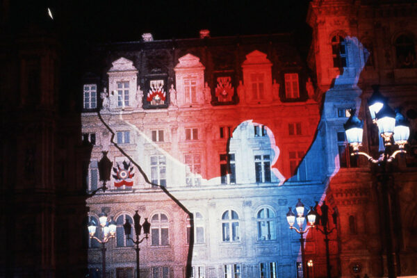 Elewacja zabytkowego budynku z wyświetloną biało-niebieską sylwetką mężczyzny z podniesionymi do góry rękoma.